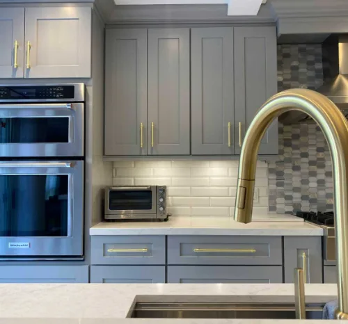 Gray CabTec Shaker cabinets with brass hardware around a pair of wall ovens